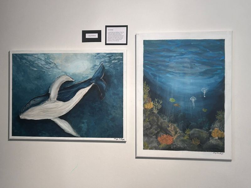 Framed whale and ocean paintings displayed at an art show