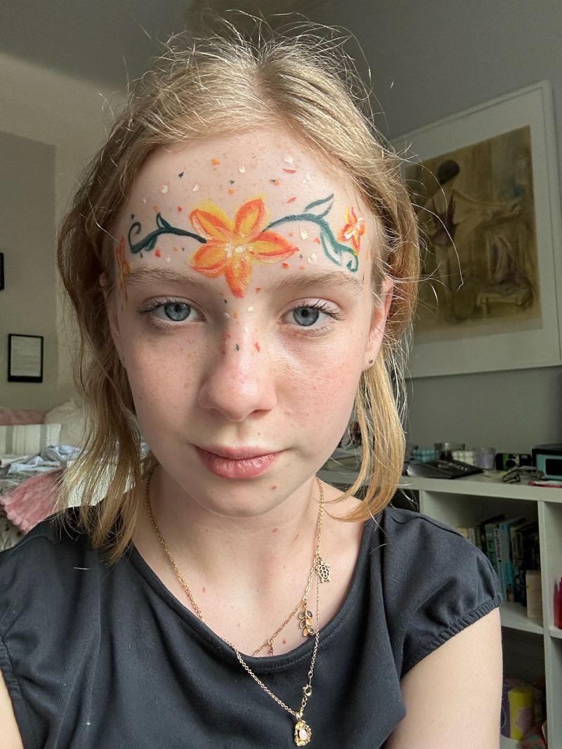 Orange and teal flower face paint on the forehead